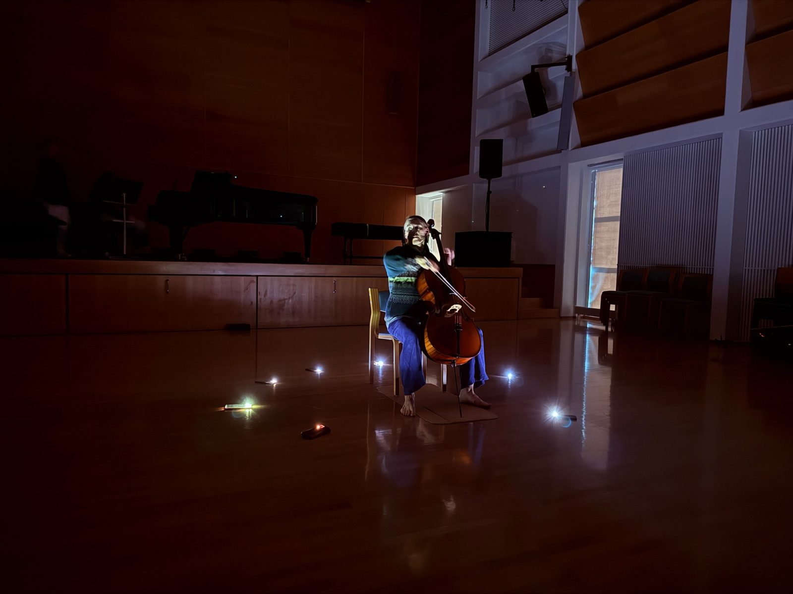 A cellist alone in the darkened hall, small lamps on the floor around her and an image projected over her